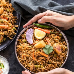 vegetable biryani in a black bowl with a bowl of yogurt on the side