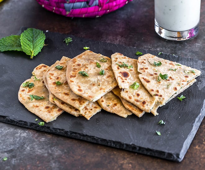 pieces of mooli paratha in a black tray with a glass of buttermilk in the background