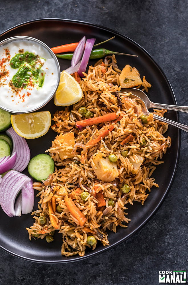 instant pot vegetable biryani in a black plate with sliced onion and lemons