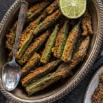 spicy bharwa bhindi in an oval brass plate, served with a side of lime