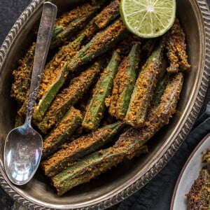 spicy bharwa bhindi in an oval brass plate, served with a side of lime