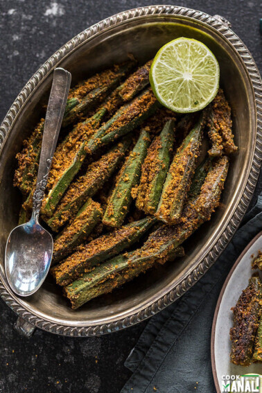spicy bharwa bhindi in an oval brass plate, served with a side of lime