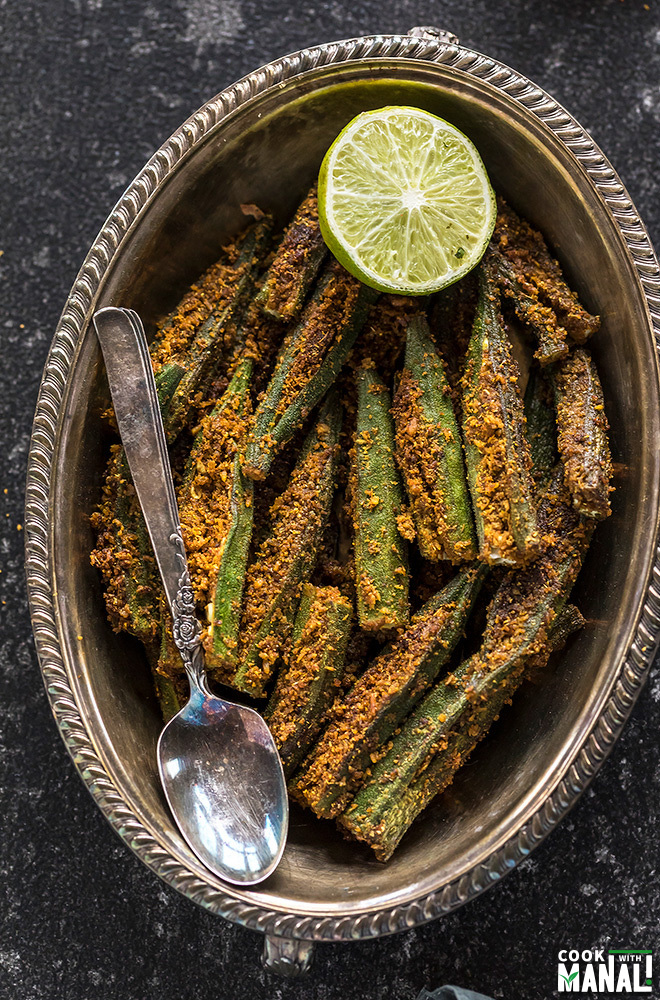 spicy bharwa bhindi in an oval brass plate, served with a side of lime