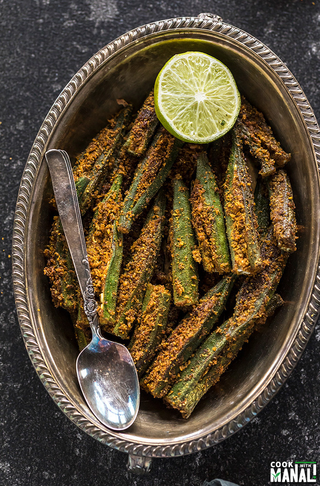 spicy bharwa bhindi in an oval brass plate, served with a side of lime