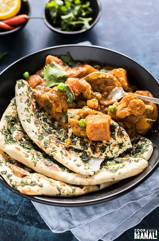 vegetable korma with naan and garnished with cilantro, served in a black bowl with a spoon