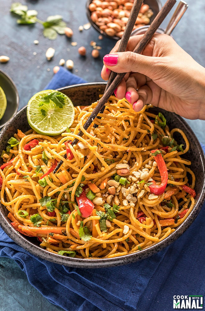 thai peanut noodles in a black bowl with a hand holding chopsticks