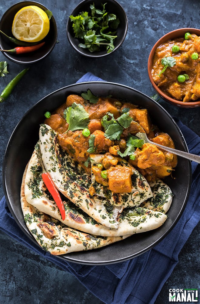 vegetable korma served along with naan in a black bowl