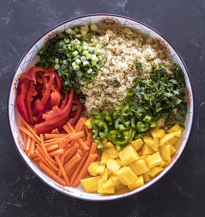 a large bowl with cooked quinoa and chopped red peppers, mango, cilantro, carrots and green onions