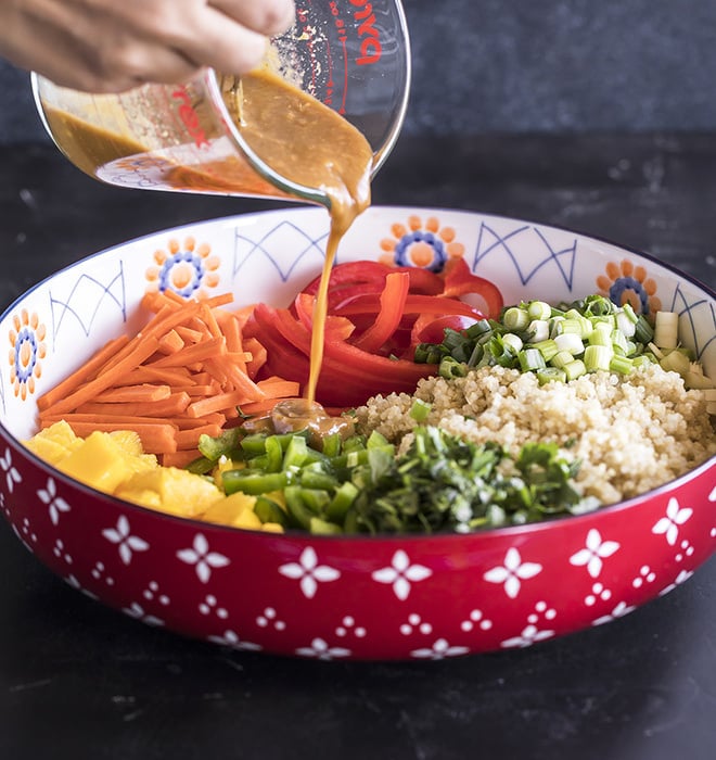 peanut ginger dressing being poured over a big bowl of quinoa salad