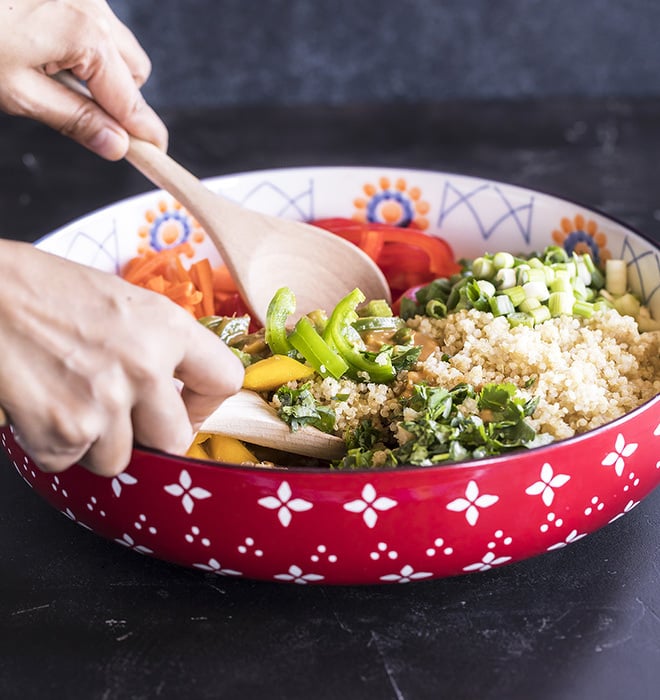 quinoa mango salad in a large bowl being tossed with two wooden spoons