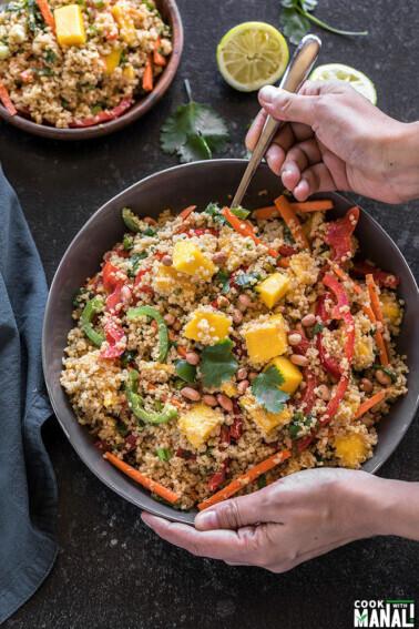 a pair of hands holding a large grey bowl of quinoa mango thai salad