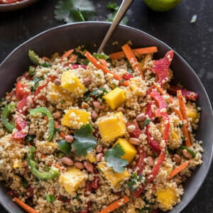 quinoa mango salad in a grey bowl with a spoon on the side