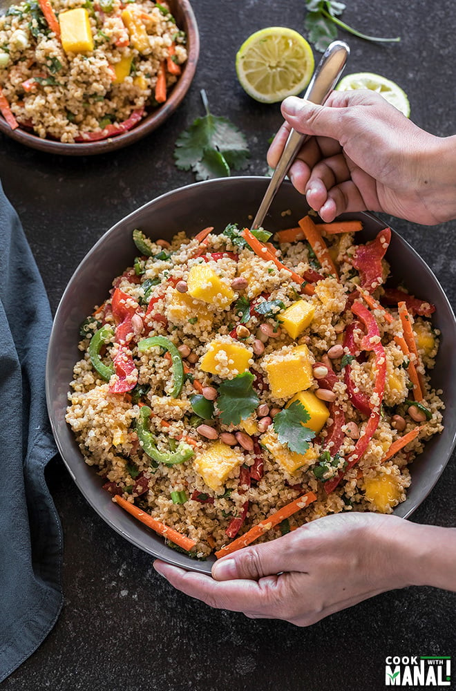 a pair of hands holding a large grey bowl of quinoa mango thai salad