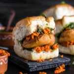 vada pav on a black coaster with chutney bowls on the back and side