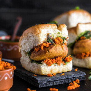 vada pav on a black coaster with chutney bowls on the back and side
