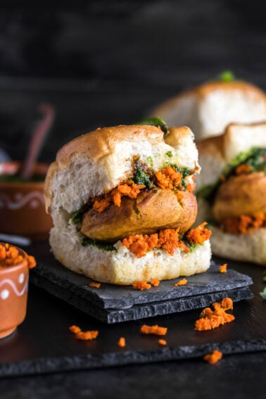 vada pav on a black coaster with chutney bowls on the back and side