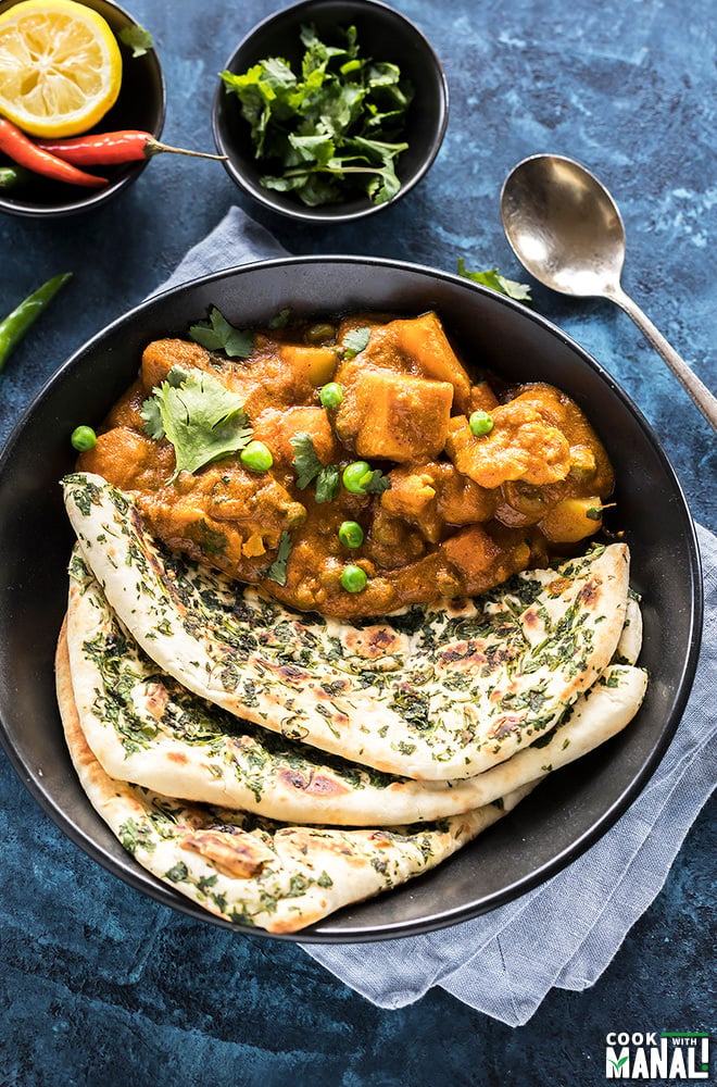 vegetable korma served along with naan in a black bowl