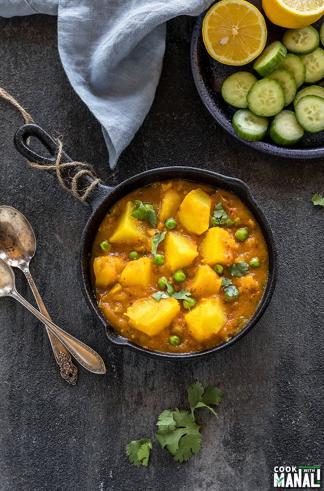 instant pot aloo matar served in a small black skillet with a plate of salad on the side