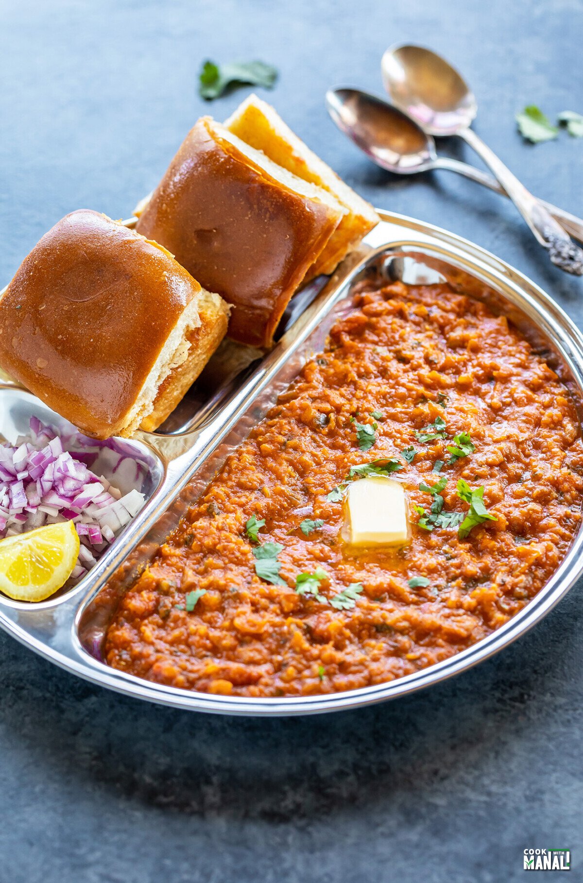 pav bhaji served in a steel plate with chopped onion and a pat of butter on top of bhaji