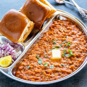 pav bhaji served in a steel plate with chopped onion and a pat of butter on top of bhaji