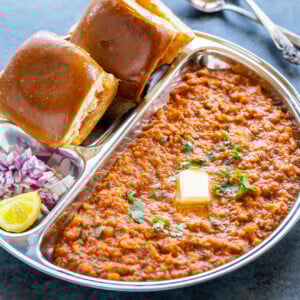 pav bhaji served in a steel plate with chopped onion and a pat of butter on top of bhaji