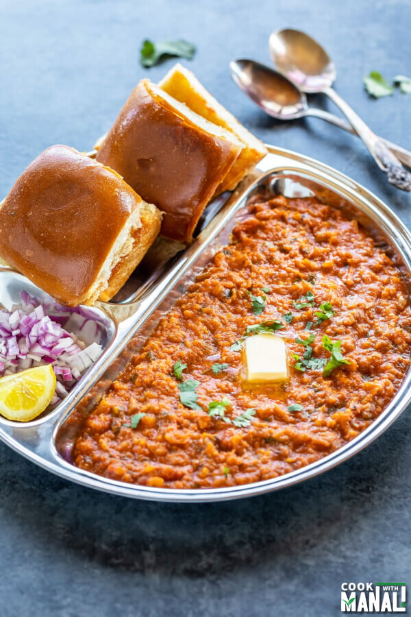 pav bhaji served in a steel plate with chopped onion and a pat of butter on top of bhaji