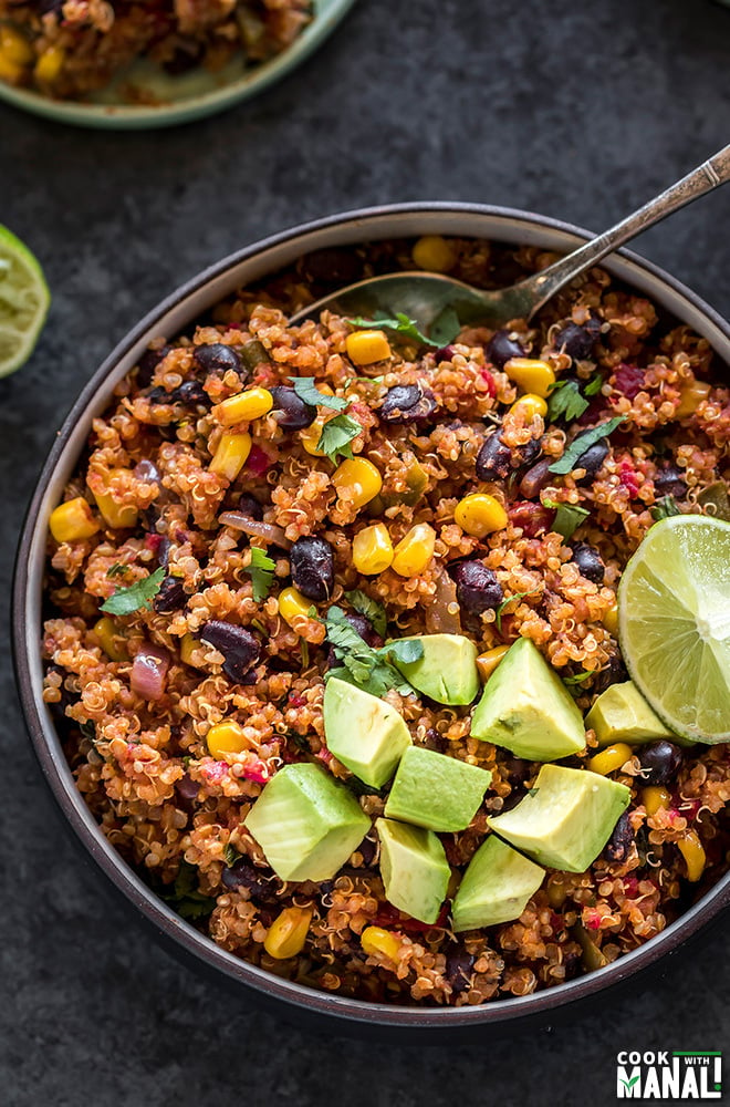 mexican quinoa in a round black bowl, garnished with diced avocados and a lime wedge