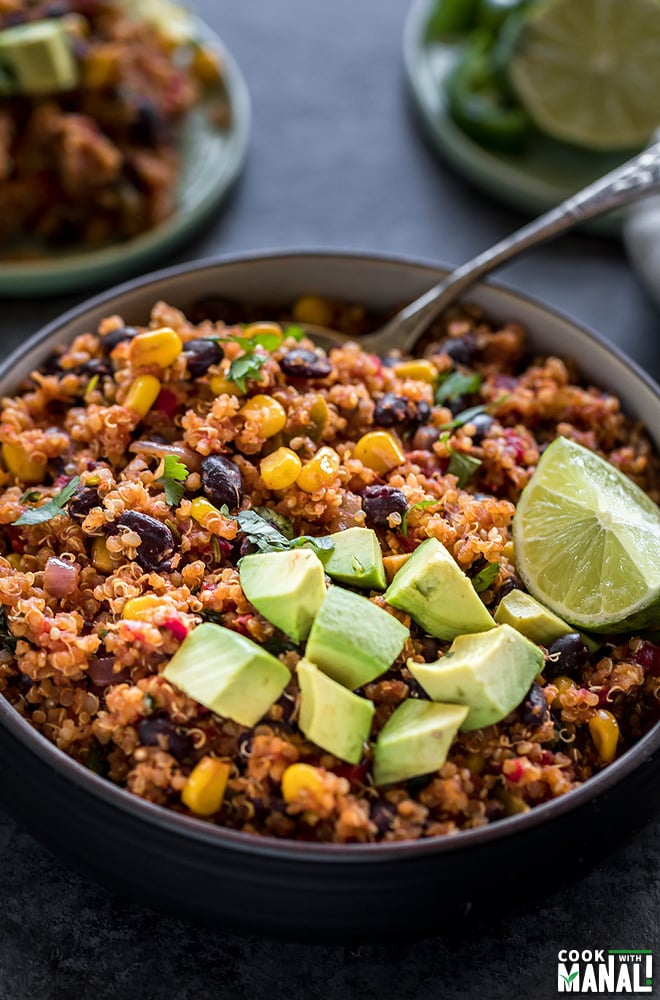 mexican quinoa in a round black bowl, garnished with diced avocados and a lime wedge