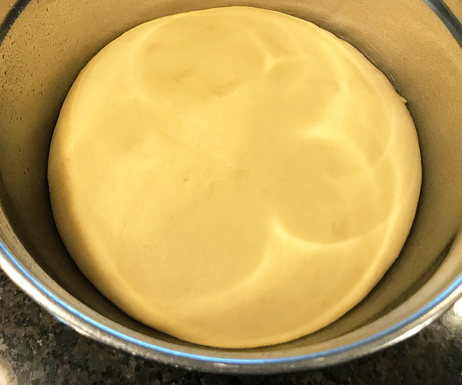 risen brioche dough in a steel bowl