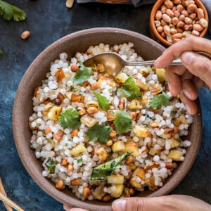 a pair of hands holding a bowl of sabudana khichdi served in a brown bowl