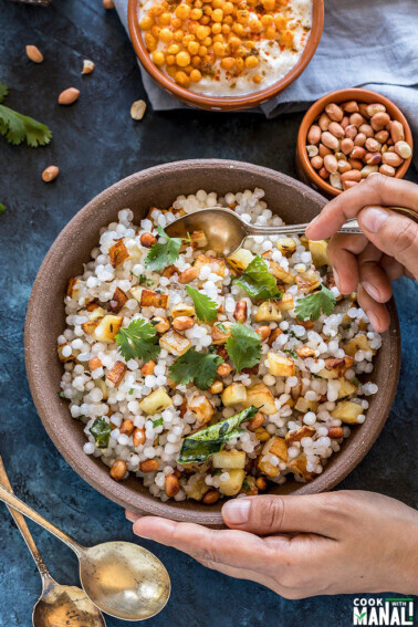 a pair of hands holding a bowl of sabudana khichdi served in a brown bowl