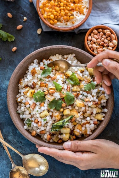 a pair of hands holding a bowl of sabudana khichdi served in a brown bowl