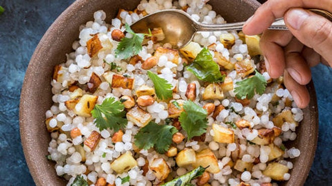 a pair of hands holding a bowl of sabudana khichdi served in a brown bowl