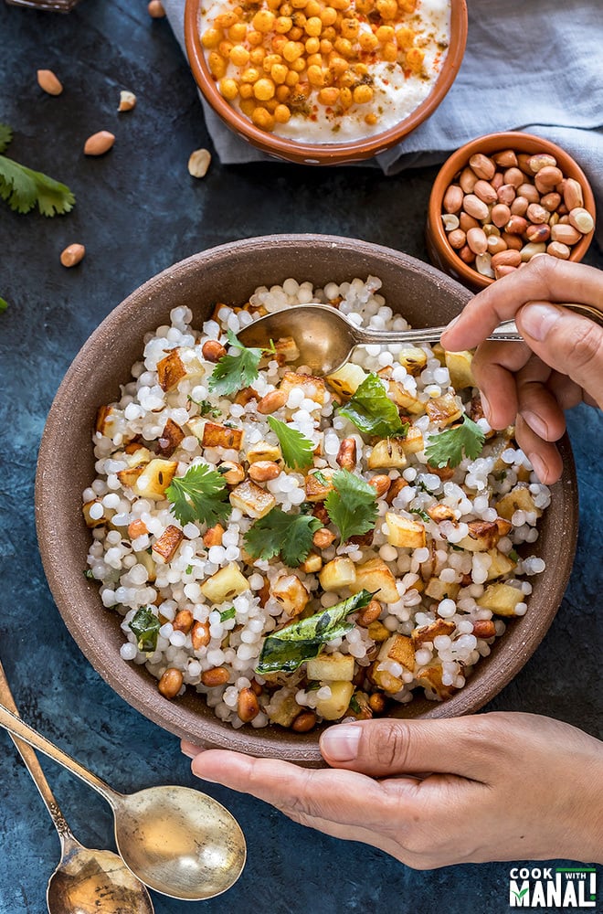 a pair of hands holding a bowl of sabudana khichdi served in a brown bowl