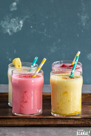 four glasses of lassi with straws in a wooden tray