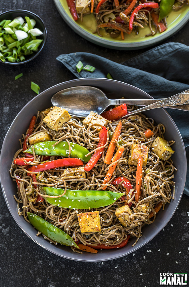 soba noodles with carrots, snow peas, tofu, red pepper in a large grey bowl with a grey napkin on the side