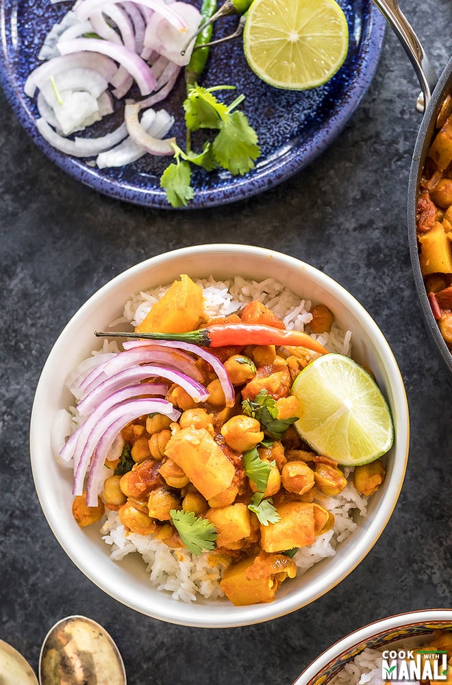 chana aloo served over rice in a bowl topped with onion, chilies and lime wedge