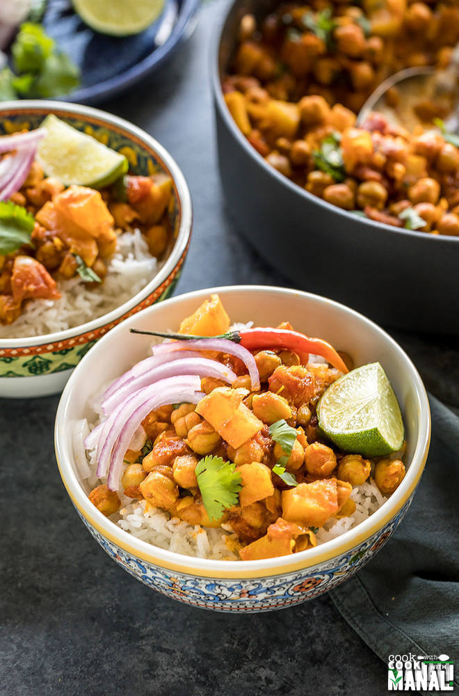 chana aloo served over rice in a bowl topped with onion, chilies and lime wedge