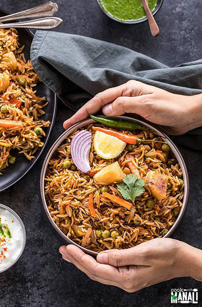 bowl of vegetable biryani held by a pair of hands