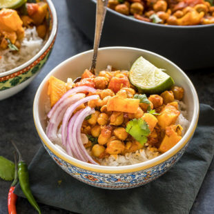 chana aloo served over rice in a bowl topped with onion, chilies and lime wedge