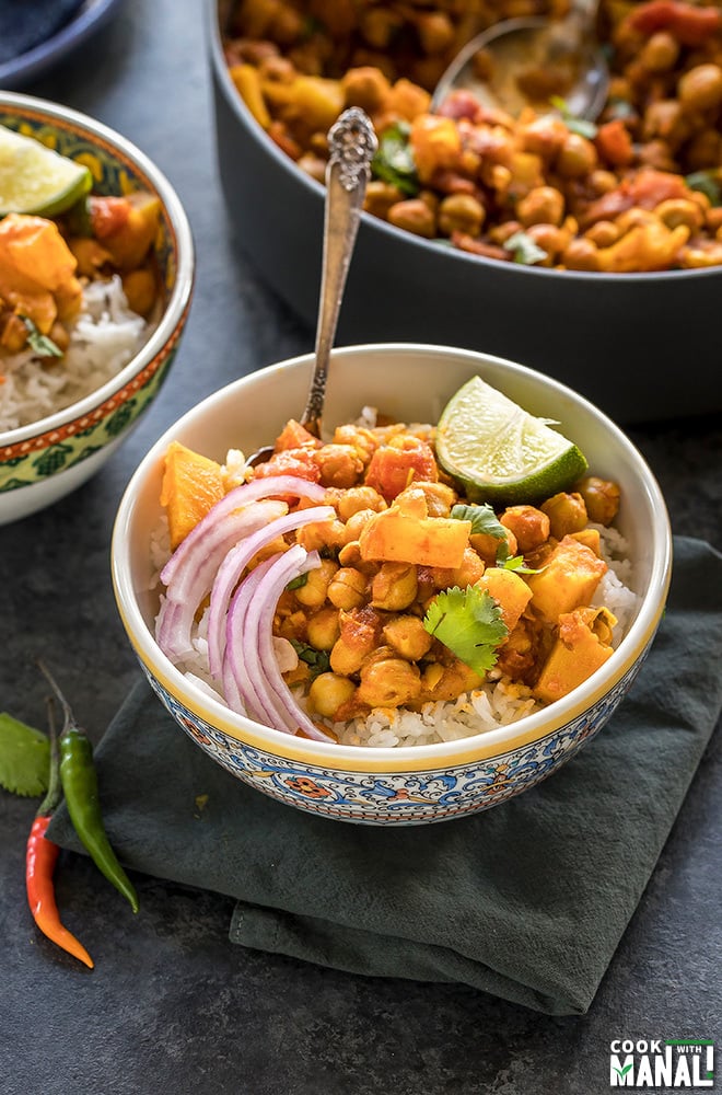 chana aloo served over rice in a bowl topped with onion, chilies and lime wedge