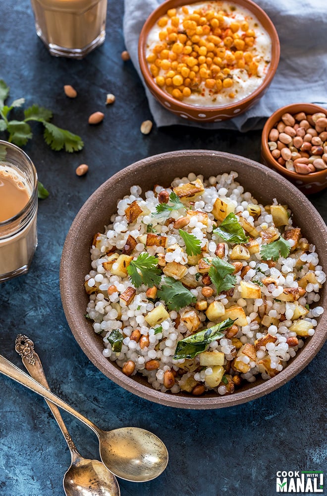 sabudana khichdi served in a brown bowl with a small bowl of yogurt in the back and a glass of chai on the side