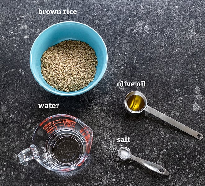 bowl of brown rice, spoon with oil and salt all placed on a board