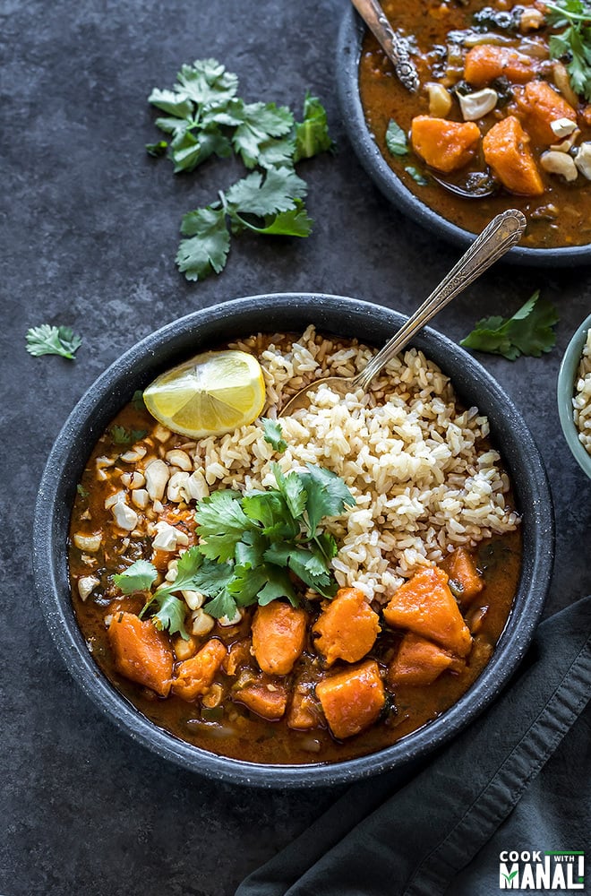 sweet potato curry and brown rice served in a black plate with cilantro on top and lemon wedge on the side