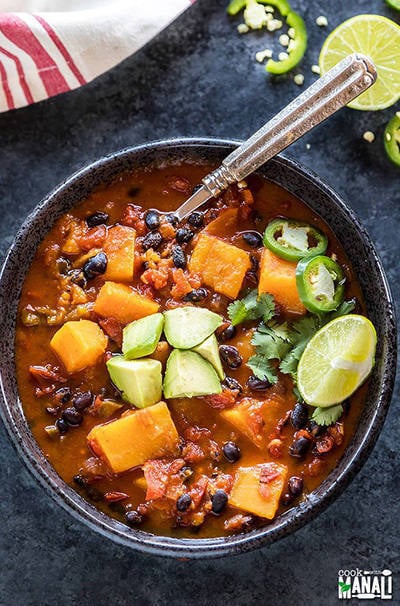 butternut squash chili in a large bowl topped with diced avocados, lime wedge and jalapenos