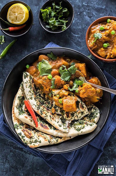 vegetable korma served in a black bowl with naan on the side