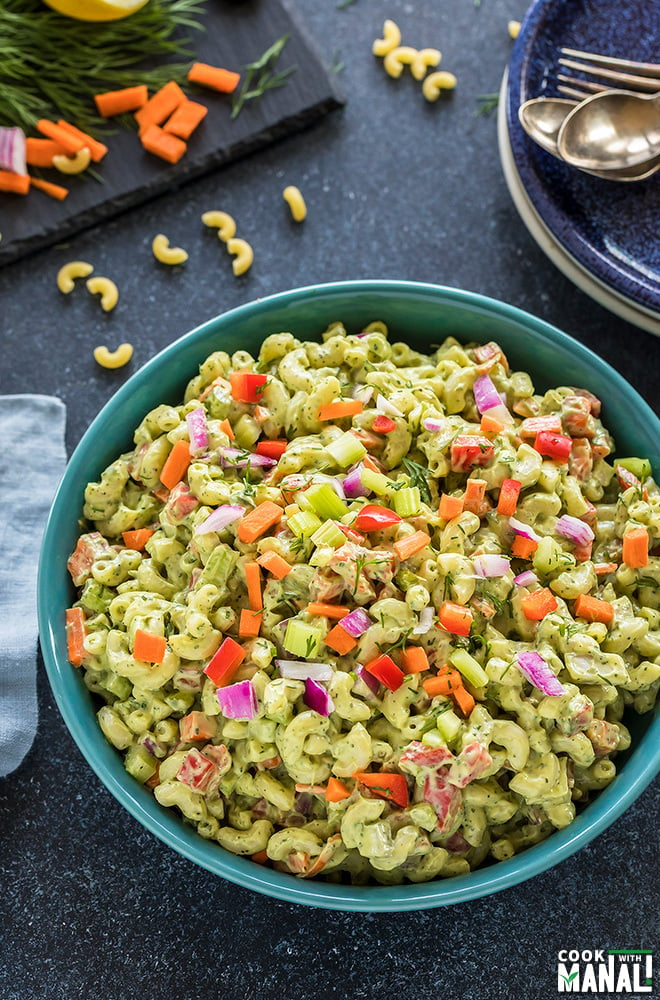 vegan macaroni salad served in a blue bowl with some plated and chopped veggies in the background