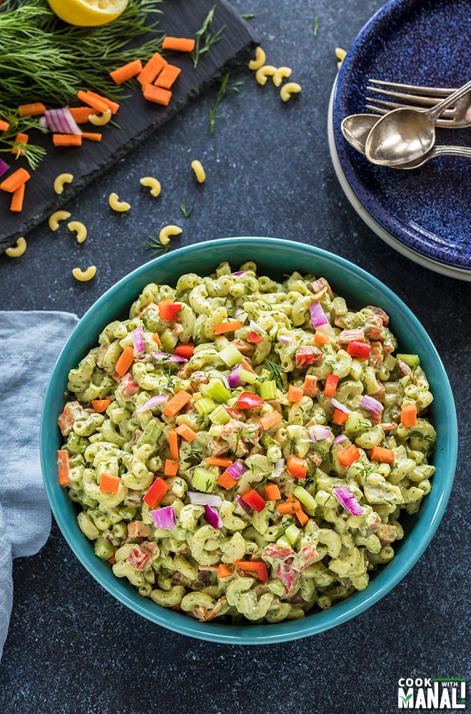 vegan macaroni salad served in a blue bowl with some plated and chopped veggies in the background