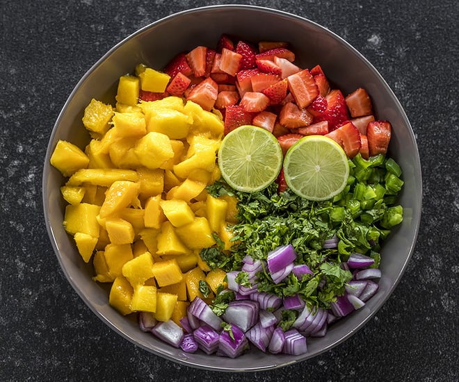 a large bowl with diced mangoes, strawberries, onion, jalapeño, cilantro and cut lime