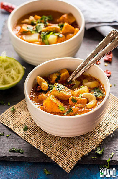 thai peanut tofu pineapple curry in a white bowl served with 2 spoons